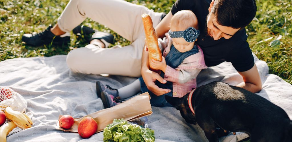 Cute family near water. Hundsome man in a green shirt. Father with little daughter. Little girl with black dog